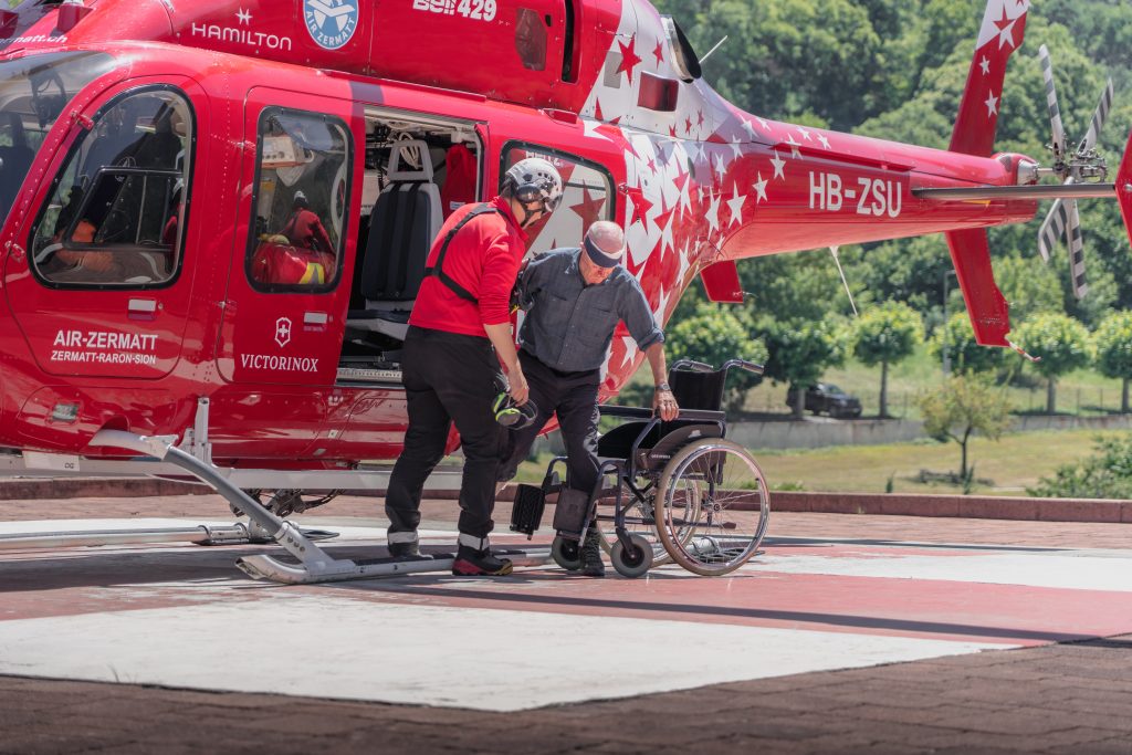 Bergretter auf Spitaldach, begleitet Patient aus Helikopter